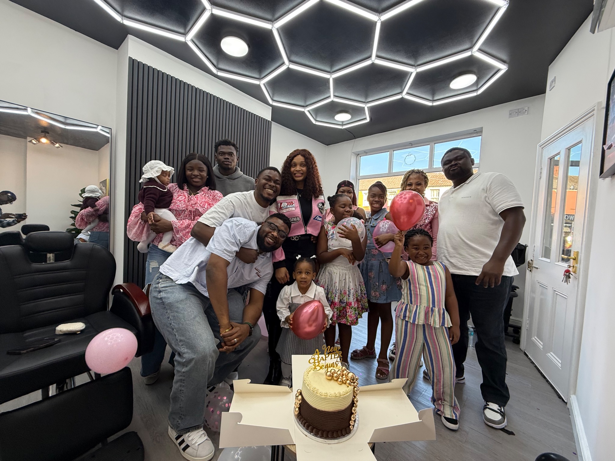 Opening-day guests smiling together around a celebration cake at MBACUTZ Hair Studio